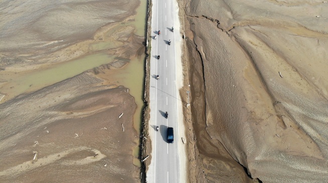 Kendaraan melintas di jalan yang berada di antara lahan pertanian yang rusak akibat terendam banjir dan lumpur banjir bandang di Pidie Jaya, Aceh, Senin (8/12/2025). [ANTARA FOTO/Irwansyah Putra/nz]
