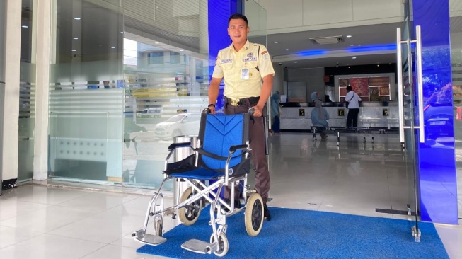 Petugas keamanan BRI Cilegon mendorong kursi roda untuk nasabah penyandang disabilitas. [Istimewa]