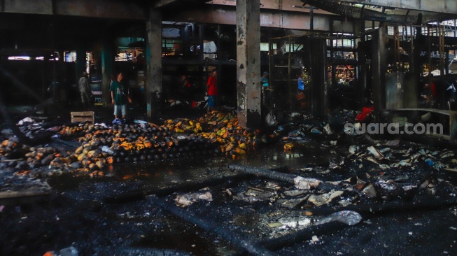 Pedagang melihat puing-puing sisa kebakaran di Pasar Induk Kramat Jati, Jakarta, Senin (15/12/2025). [Suara.com/Alfian Winanto]