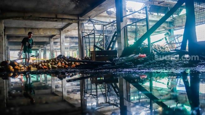 Pedagang melihat puing-puing sisa kebakaran di Pasar Induk Kramat Jati, Jakarta, Senin (15/12/2025). [Suara.com/Alfian Winanto]