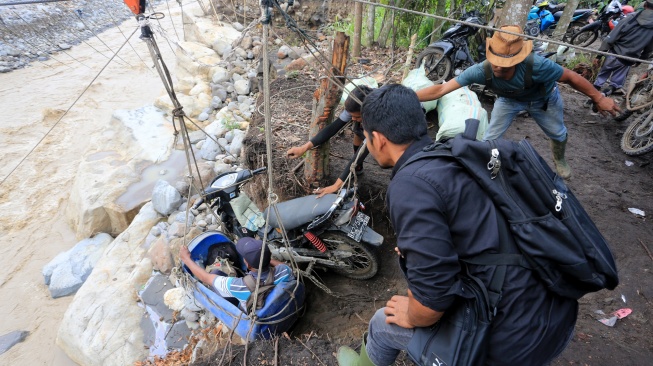 Warga membantu korban bencana yang terisolir saat menaiki derek pengangkut barang untuk melintasi Daerah Aliran Sungai (DAS) Peusangan dari Desa Bergang Kecamatan Ketol, Aceh Tengah dan Desa Simpang Rahmat, Gajah Putih, Bener Meriah, Aceh, Minggu (14/12/2025). [ANTARA FOTO/Syifa Yulinnas/nz]