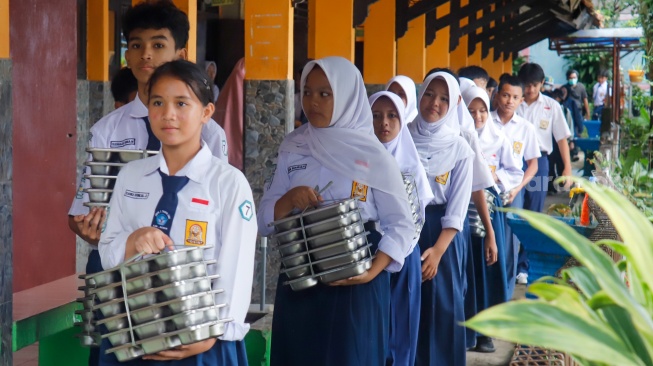 Para siswa membawa menu Makan Bergizi Gratis (MBG) untuk dibagikan ke kelas masing-masinh di SMPN 1 Tamansari, Bogor, Jawa Barat, Selasa (16/12/2025). [Suara.com/Alfian Winanto]
