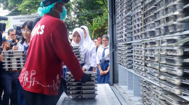 Petugas mendistribusikan menu Makan Bergizi Gratis (MBG) di SMPN 1Tamansari, Bogor, Selasa (16/12/2025). [Suara.com/Alfian Winanto]