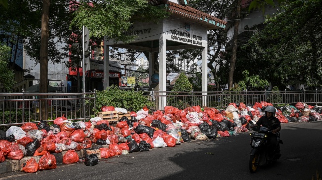 Pengendara sepeda motor melintas di dekat tumpukan sampah di Jalan Kihajar Dewantara, Ciputat, Tangerang Selatan, Banten, Sabtu (13/12/2025). [ANTARA FOTO/Sulthony Hasanuddin/tom]