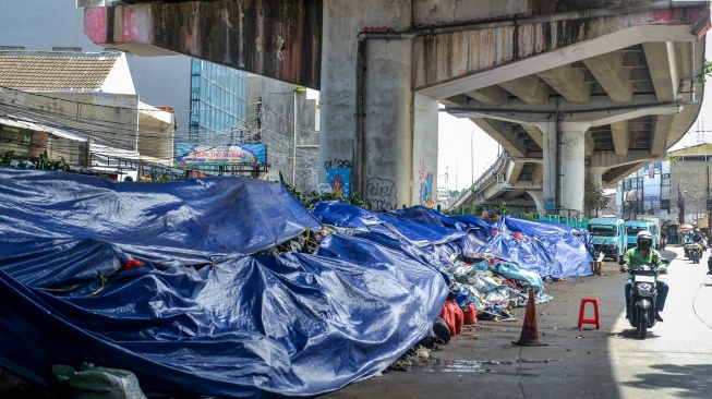 Pengendara motor melintas di samping tumpukan sampah yang ditutupi terpal di Ciputat, Tangerang Selatan, Banten, Selasa (16/12/2025). [ANTARA FOTO/Putra M. Akbar/foc]