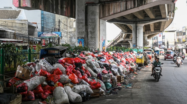 Pengendara sepeda motor menutup hidungnya saat melintas di dekat tumpukan sampah di Jalan Dewi Sartika, Ciputat, Tangerang Selatan, Banten, Sabtu (13/12/2025). [ANTARA FOTO/Sulthony Hasanuddin/tom]