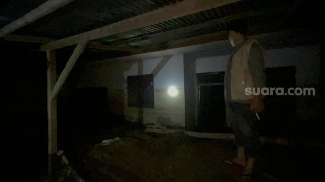 Mukhlis, warga Gampong Dayah Husein, Meurah Dua, Pidie Jaya, saat menunjukkan kondisi rumahnya yang terkubur lumpur, Senin (15/12/2025) malam. [Suara.com/Iskandar]