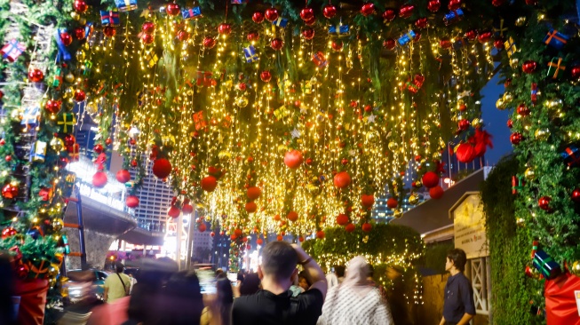 Warga melihat instalasi pencahayaan pada Jakarta Light Festival 2025 di kawasan Bundaran HI, Jakarta, Selasa (23/12/2025). [Suara.com/Alfian Winanto]
