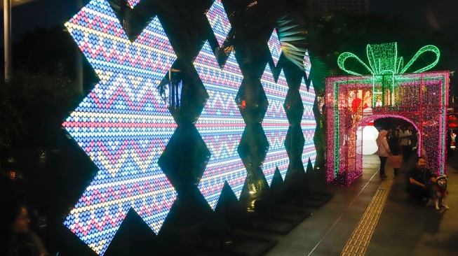 Warga melihat instalasi pencahayaan pada Jakarta Light Festival 2025 di kawasan Bundaran HI, Jakarta, Selasa (23/12/2025). [Suara.com/Alfian Winanto]
