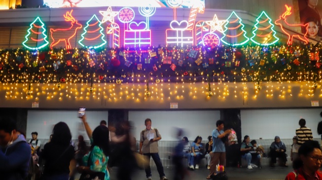Warga melihat instalasi pencahayaan pada Jakarta Light Festival 2025 di kawasan Bundaran HI, Jakarta, Selasa (23/12/2025). [Suara.com/Alfian Winanto]

