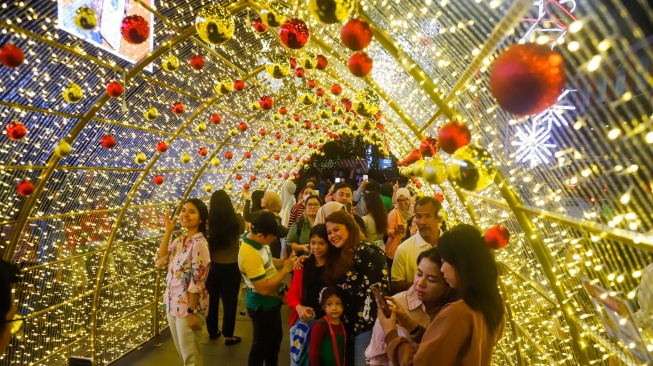 Warga melihat instalasi pencahayaan pada Jakarta Light Festival 2025 di kawasan Bundaran HI, Jakarta, Selasa (23/12/2025). [Suara.com/Alfian Winanto]
