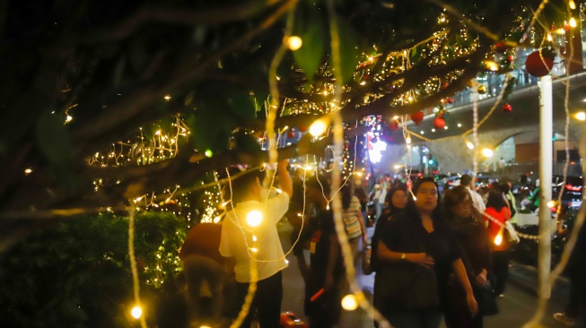 Warga melihat instalasi pencahayaan pada Jakarta Light Festival 2025 di kawasan Bundaran HI, Jakarta, Selasa (23/12/2025). [Suara.com/Alfian Winanto]
