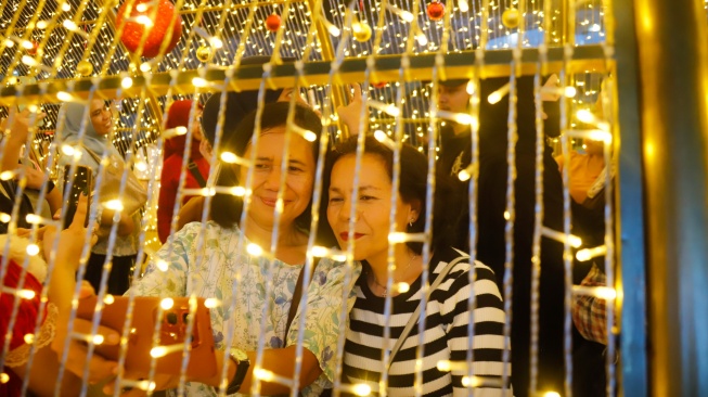 Warga berswafoto saat melihat instalasi pencahayaan pada Jakarta Light Festival 2025 di kawasan Bundaran HI, Jakarta, Selasa (23/12/2025). [Suara.com/Alfian Winanto]
