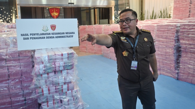 Petugas dari Kejaksaan Agung melintas di tengah tumpukan uang hasil penagihan denda administratif kehutanan dan penyelamatan keuangan negara dari hasil tindak pidana korupsi di kompleks Kejaksaan Agung, Jakarta, Rabu (24/12/2025). [ANTARA FOTO/Aditya Pradana Putra/sgd]