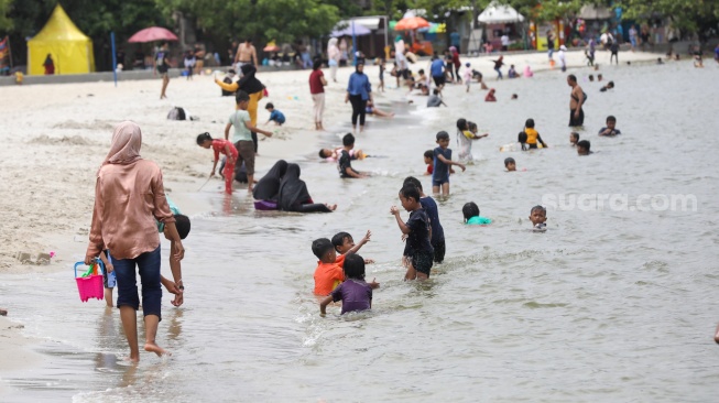 Pengunjung berwisata di Pantai Lagoon, Taman Impian Jaya Ancol, Jakarta, Jumat (26/12/2025). [Suara.com/Alfian Winanto]