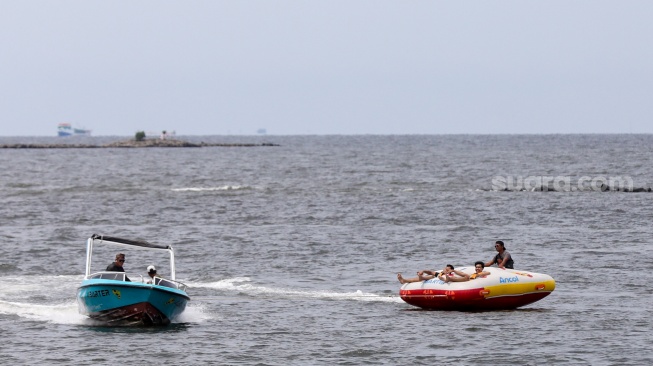 Pengunjung berwisata di Pantai Lagoon, Taman Impian Jaya Ancol, Jakarta, Jumat (26/12/2025). [Suara.com/Alfian Winanto]