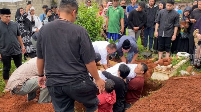Gilang Dirga ikut turun ke liang lahad dan mengazankan jenazah ayahnya, Wendi Indra bin Muhammad Yasin meninggal dunia pada Rabu, 31 Desember 2025 dini hari. Jenazakh dimakamnkan di TPU Al Hidayah, Pondok Gede, Bekasi, Jawa Barat pada pagi tadi. [Tiara Rosana/Suara.com]