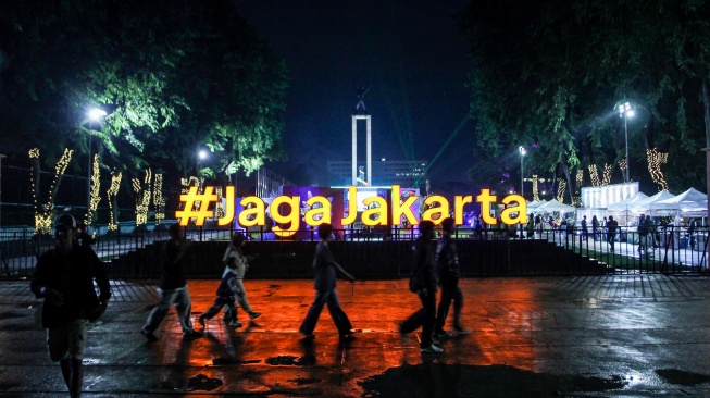 Warga melintasi instalasi pencahayaan Jaga Jakarta saat perayaan malam Tahun Baru 2026 di Lapangan Banteng, Jakarta, Rabu (31/12/2025). [ANTARA FOTO/Naufal Khoirulloh/wpa]
