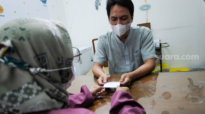 Dokter memberikan kartu vaksinasi kepada pasien di Klinik Pratama Dermaga Raya, Jakarta, Rabu (7/1/2026). [Suara.com/Alfian Winanto]