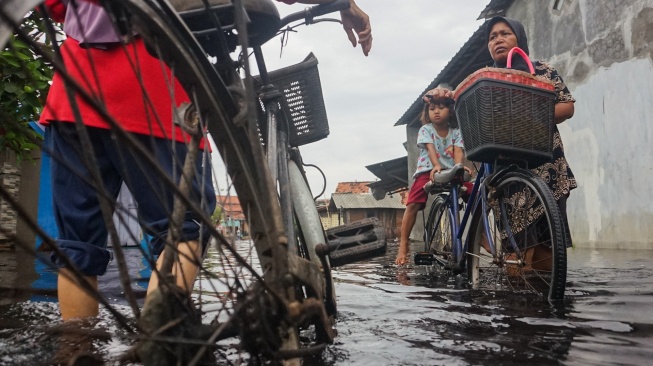 Warga mendorong sepedanya melewati jalan perkampungan yang tergenang banjir di Pabean, Kota Pekalongan, Jawa Tengah, Rabu (7/1/2026). [ANTARA FOTO/Harviyan Perdana Putra/foc]
