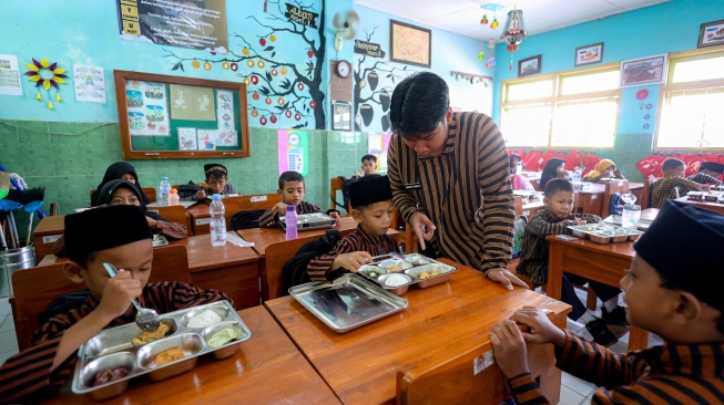 Petugas menjelaskan kandungan gizi kepada siswa saat mendistribusikan paket makanan menu kuliner nusantara untuk program Makan Bergizi Gratis (MBG) di SD Negeri Tanjunganom 3, Nganjuk, Jawa Timur, Kamis (8/1/2026). [ANTARA FOTO/Muhammad Mada/nz]