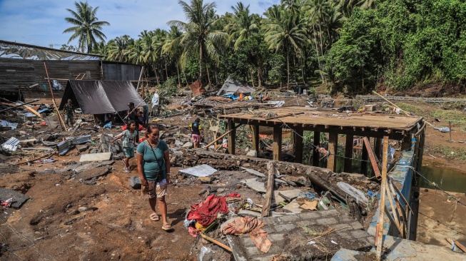 Sejumlah warga melintas di depan rumah yang rusak pascabanjir di Desa Tongute Ternate asal Kabupaten Halmahera Barat, Maluku Utara, Kamis (8/1/2026). [ANTARA FOTO/Andri Saputra/tom]
