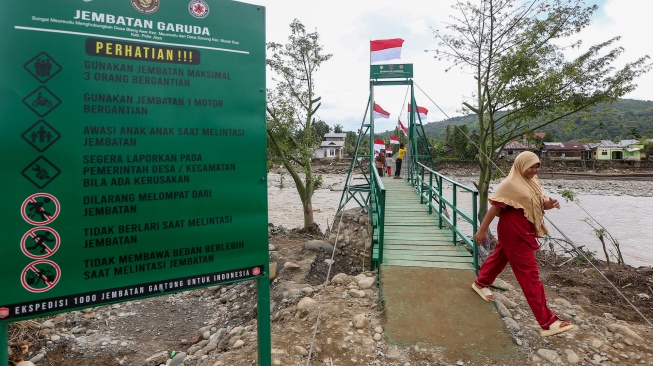 Warga dan pelajar melintas di atas jembatan gantung yang baru selesai pembangunannya di Meureudu, Pidie Jaya, Aceh, Jumat (9/1/2026).  [ANTARA FOTO/Irwansyah Putra/bar]