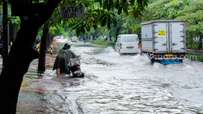 Pengendara mendorong motornya melewati banjir yang menggenang di Jalan Danau Sunter Raya, Jakarta, Senin (12/1/2026). [Suara.com/Alfian Winanto]