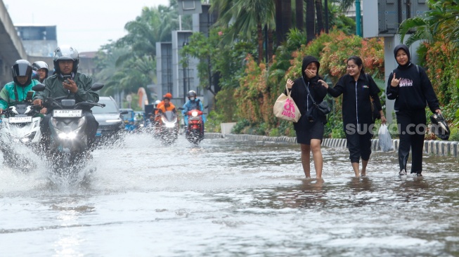 Warga berjalan melewati banjir yang menggenang di Jalan Boulevard Raya, Kelapa Gading, Jakarta, Senin (12/1/2026). [Suara.com/Alfian Winanto]