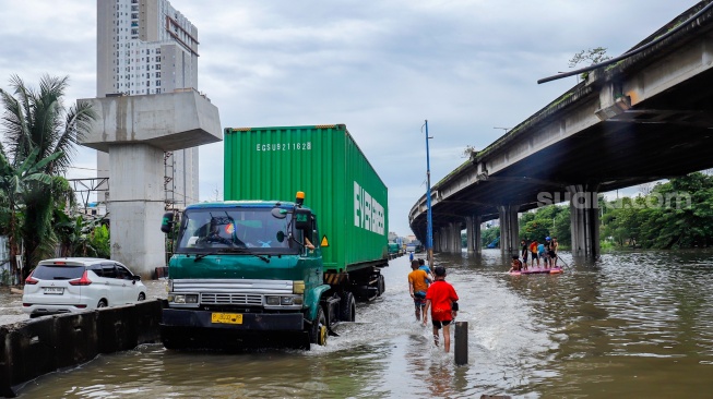 Kendaraan truk melewati banjir yang menggenang di Jalan RE Martadinata, Tanjung Priok, Jakarta, Senin (12/1/2026). [Suara.com/Alfian Winanto]