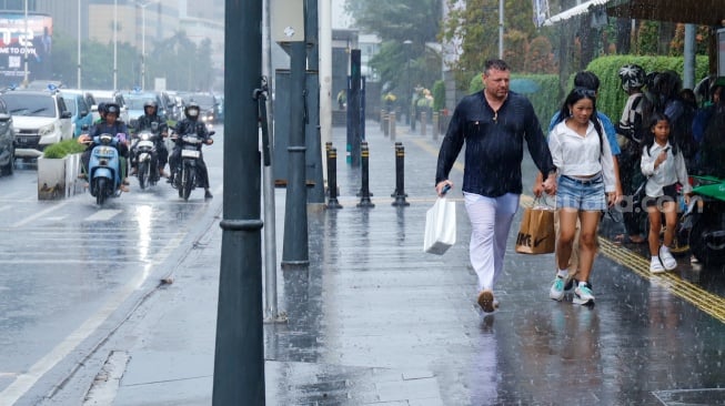 Sejumlah warga beraktivitas saat turun hujan di kawasan Bundaran HI, Jakarta, Selasa (13/1/2026). [Suara.com/Alfian Winanto]
