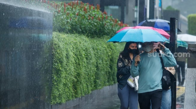 Sejumlah warga beraktivitas saat turun hujan di kawasan Bundaran HI, Jakarta, Selasa (13/1/2026). [Suara.com/Alfian Winanto]
