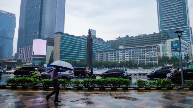 Sejumlah warga beraktivitas saat turun hujan di kawasan Bundaran HI, Jakarta, Selasa (13/1/2026). [Suara.com/Alfian Winanto]
