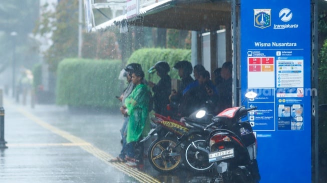Sejumlah warga beraktivitas saat turun hujan di kawasan Bundaran HI, Jakarta, Selasa (13/1/2026). [Suara.com/Alfian Winanto]
