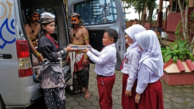 Relawan Satuan Pelayanan Pemenuhan Gizi (SPPG) Danupayan berpakaian seni Warokan saat membagikan paket makan bergizi gratis (MBG) kepada pelajar SD Negeri Pandemulyo di Bulu, Temanggung, Jawa Tengah, Senin (19/1/2026). [ANTARA FOTO/Anis Efizudin/wsj]