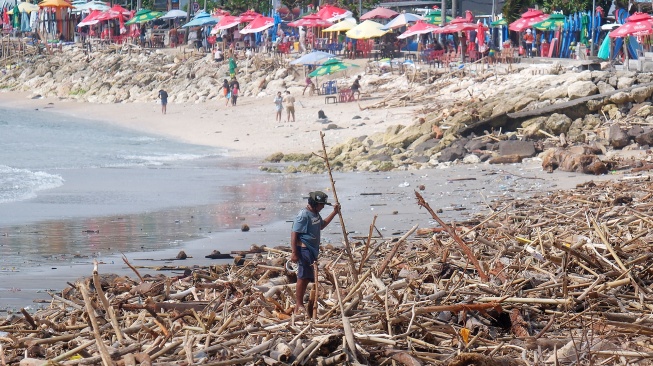 Seorang warga berdiri di atas tumpukan sampah kiriman di Pantai Kuta, Badung, Bali, Senin (19/1/2026). [ANTARA FOTO/Nyoman Hendra Wibowo/tom]