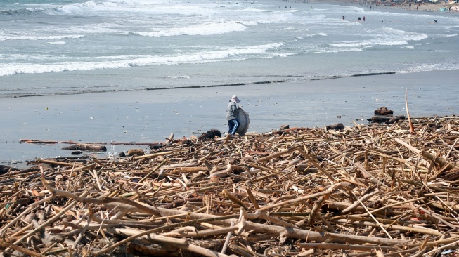 Seorang warga berdiri di atas tumpukan sampah kiriman di Pantai Kuta, Badung, Bali, Senin (19/1/2026). [ANTARA FOTO/Nyoman Hendra Wibowo/tom]