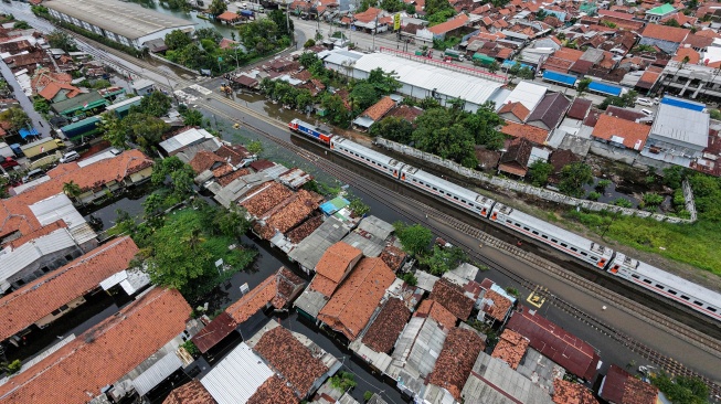 Foto udara kereta api melintas dengan kecepatan terbatas melewati jalur rel kereta yang terdampak banjir di sekitar Stasiun Pekalongan, Kota Pekalongan, Jawa Tengah, Rabu (21/1/2026). [ANTARA FOTO/Harviyan Perdana Putra/wsj]

