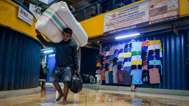 Buruh angkut berjalan melewati genangan air di Pasar Cipulir, Jakarta, Kamis (22/1/2026). [ANTARA FOTO/Putra M. Akbar/agr]