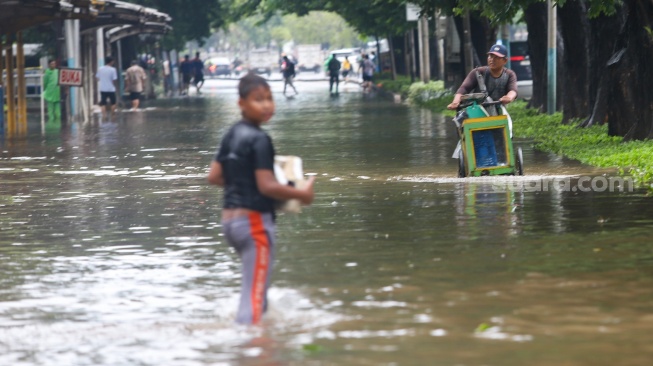 Warga beraktivitas di tengah genangan banjir yang merendam di sekitar Cempaka Putih, Jakarta, Kamis (22/1/2026). [Suara.com/Alfian Winanto]
