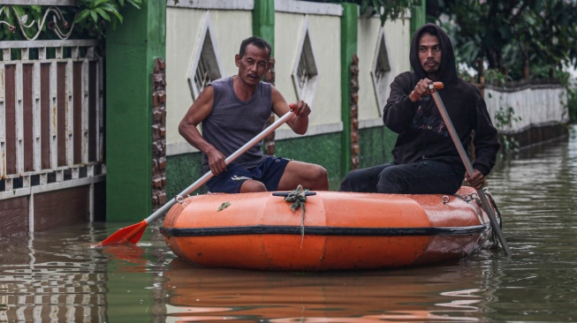 Dua warga menggunakan perahu untuk melintasi permukiman yang terendam banjir di Desa Karangligar, Telukjambe, Karawang, Jawa Barat, Kamis (22/1/2026). [ANTARA FOTO/Darryl Ramadhan/app/tom]