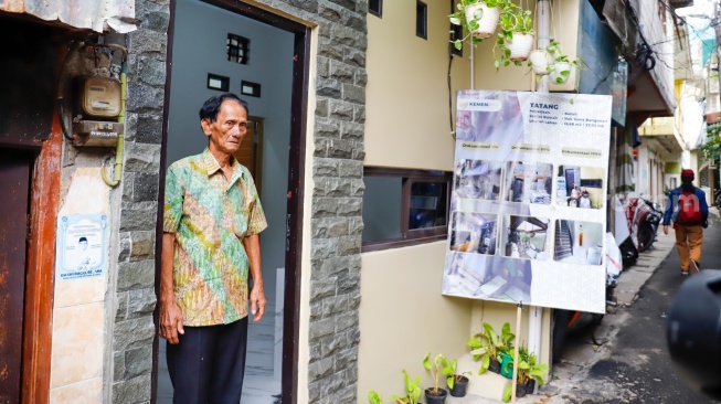 Warga berdiri di depan rumahnya yang sudah direnovasi di perkampungan padat penduduk, kawasan Menteng Tenggulun, Jakarta, Rabu (28/1/2026). [Suara.com/Alfian Winanto]