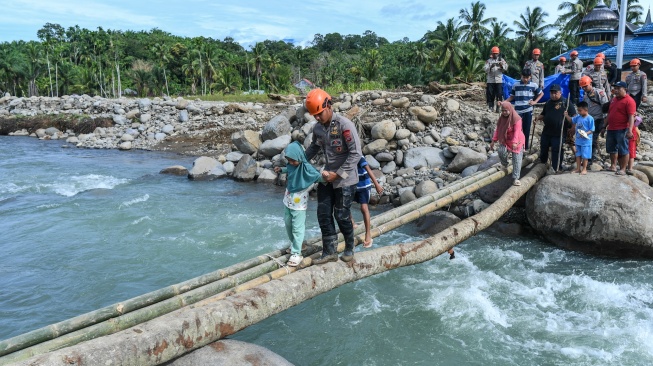 Polisi membantu penyintas bencana menyeberangi jembatan darurat di Jorong Kayu Pasak Selatan, Nagari Salareh Aia, Palembayan, Agam, Sumatera Barat, Rabu (18/2/2026). [ANTARA FOTO/Wahdi Septiawan/YU]