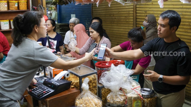 Pedagang melayani pembeli kue kering yang dijual di Pasar Jatinegara, Jakarta, Senin (9/3/2026). [Suara.com/Alfian Winanto]