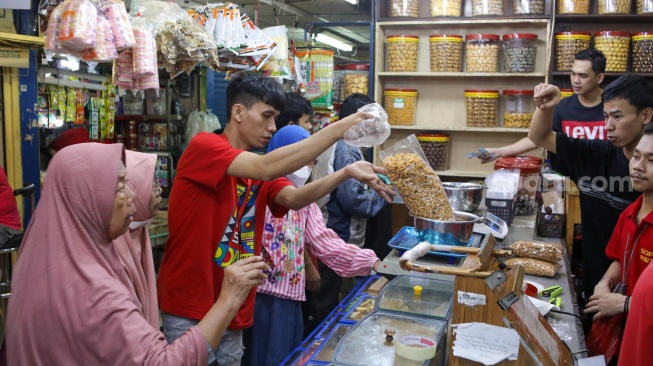 Pedagang melayani pembeli kue kering yang dijual di Pasar Jatinegara, Jakarta, Senin (9/3/2026). [Suara.com/Alfian Winanto]