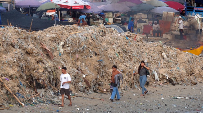 Sejumlah warga berjalan di dekat tumpukan sampah kiriman yang menggunung di Pantai Kedonganan, Badung, Bali, Kamis (26/3/2026). [ANTARA FOTO/Nyoman Hendra Wibowo/bar]