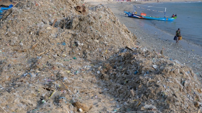 Seorang nelayan berjalan di dekat tumpukan sampah kiriman yang menggunung di Pantai Kedonganan, Badung, Bali, Kamis (26/3/2026). [ANTARA FOTO/Nyoman Hendra Wibowo/bar]