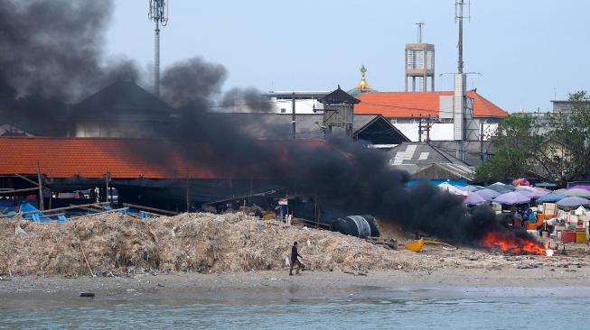 Seorang warga berjalan di dekat tumpukan sampah kiriman yang menggunung di Pantai Kedonganan, Badung, Bali, Kamis (26/3/2026). [ANTARA FOTO/Nyoman Hendra Wibowo/bar]