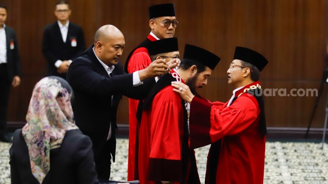 Ketua Hakim Konstitusi Suhartoyo (kanan) melepaskan kalung jabatan Anwar Usman saat acara Wisuda Purnabakti dan Penyambutan Hakim di Gedung Mahkamah Konstitusi, Jakarta, Senin (13/4/2026). [Suara.com/Alfian Winanto]
