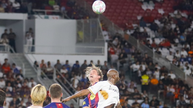 Pemain DRX World Legends, Makelele berebut bola dengan pemain Barca Legends, Phillip Cocu saat pertandingan sepak bola Clash of Legends antara Barca Legends vs DRX World Legends di Stadion Utama Gelora Bung Karno (SUGBK), Jakarta, Sabtu (18/4/2026). [Suara.com/Alfian Winanto]